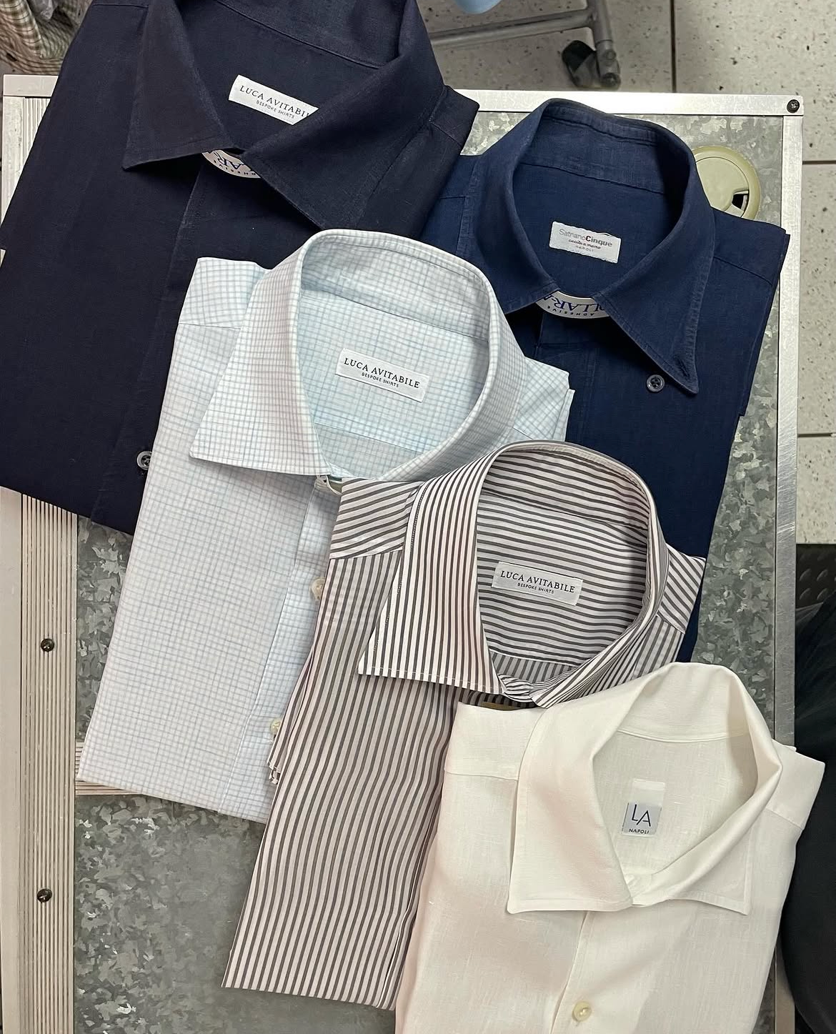 Five freshly pressed bespoke shirts folded on the pressing table at Express Ironing